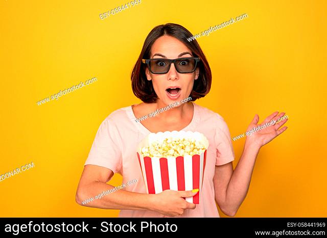 young woman with a bucket of popcorn in stereo glasses. with short hair on a yellow background High quality photo