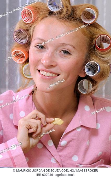 Redheaded woman wearing pajamas with curlers in her hair eating biscuit