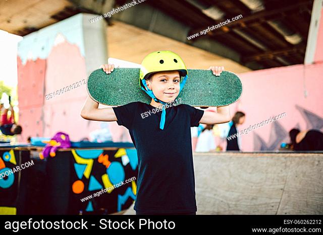 Portrait boy holding skateboard over shoulder. Beautiful kid model posing on skate board park. Portrait stylish child with skate board on half pipe ramp an...