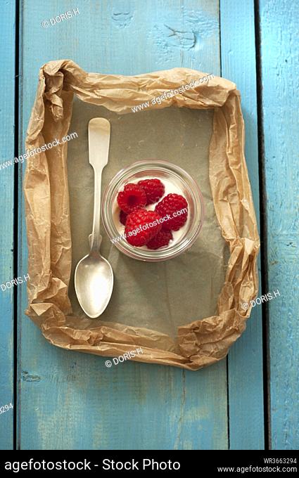 Glass of yoghurt with raspberries on wooden table, close up