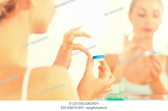 beauty, vision, eyesight, ophthalmology and people concept - close up of young woman applying contact lenses at mirror in home bathroom