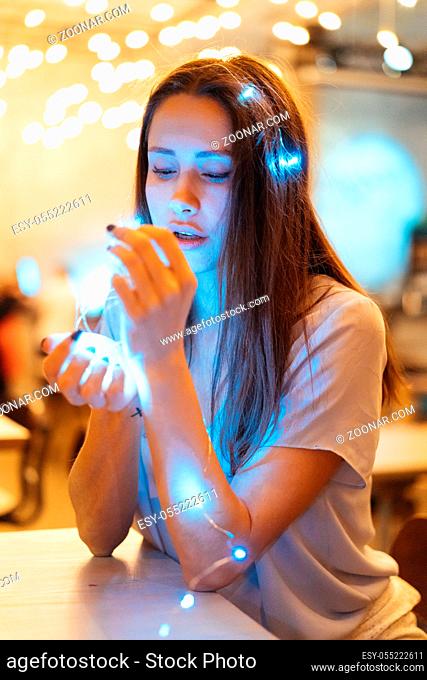 Portrait of beautiful brunette woman holding glowing christmas garland in hands