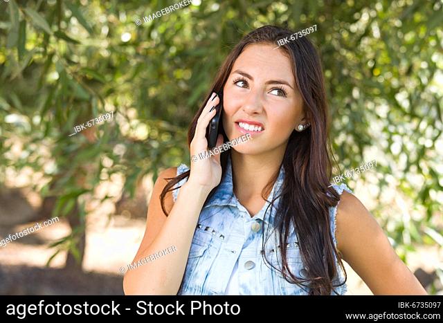Unhappy, confused mixed-race young female talking on cell phone outside