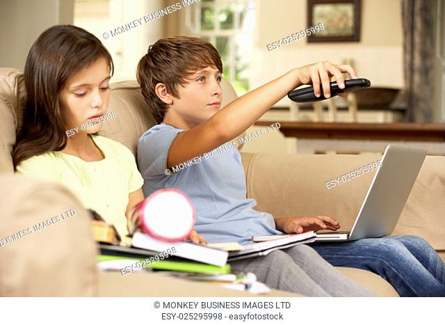 Two Children Distracted By Television Whilst trying To Do With Homework