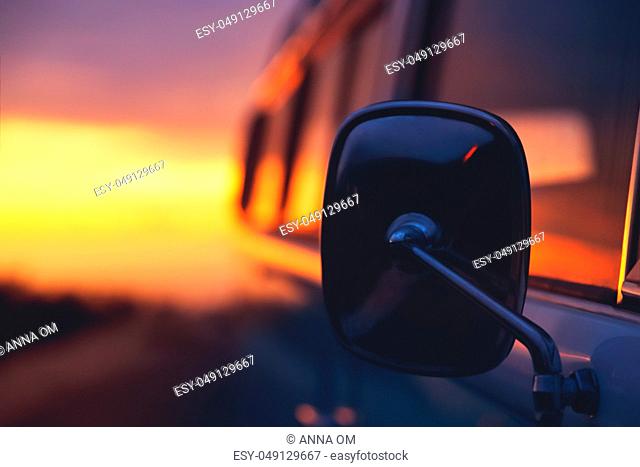 Travels in camper van, closeup photo of side view mirror over sunset background, adventurous journey in the house on the wheels, freedom and recreation concept
