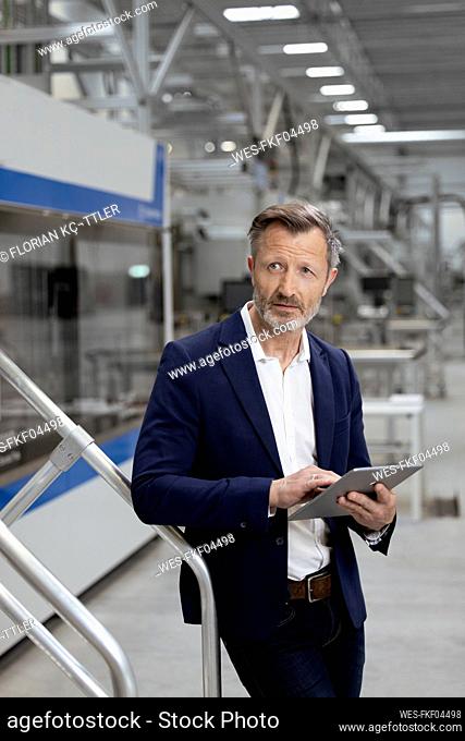 Male professional with digital tablet leaning on railing in factory