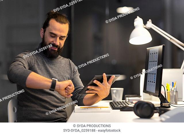 man with smartwatch and tablet pc at night office