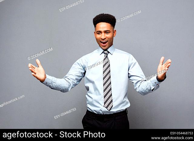 Business Concept - Confident cheerful young African American showing hands in front of him with surprising expression over grey background