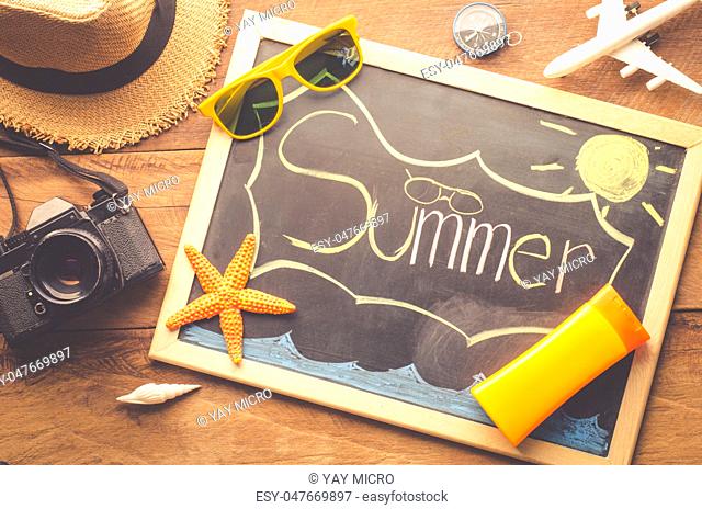 Sea travel accessories A hat, sunglasses, camera. Placed on wooden with word 'SUMMER"" on blackboard