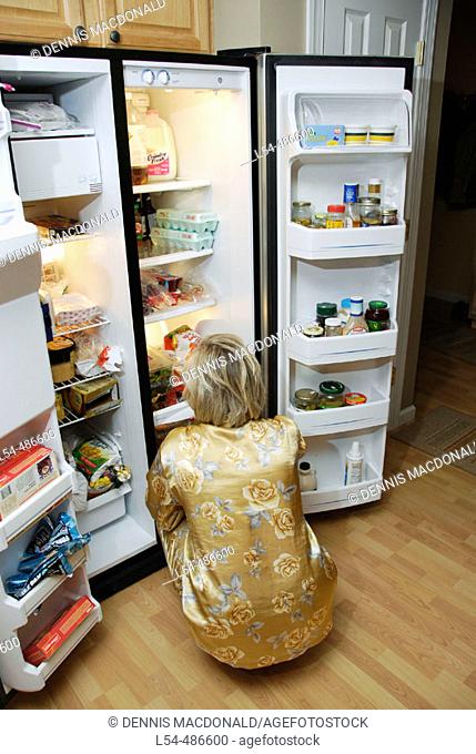 Adult woman looks through the refriderator for a late night snack