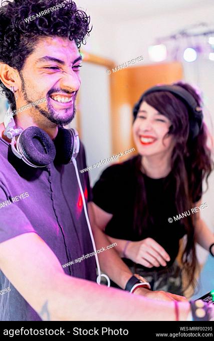 Cheerful young male musician with female DJ enjoying while mixing sound at recording studio