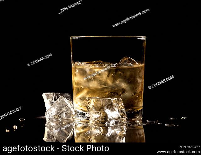 Glass of scotch and ice cubes on black background