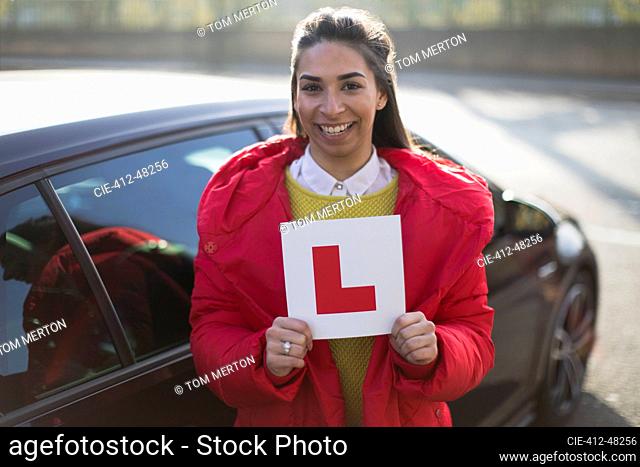 Portrait confident, happy young woman holding learners permit by car