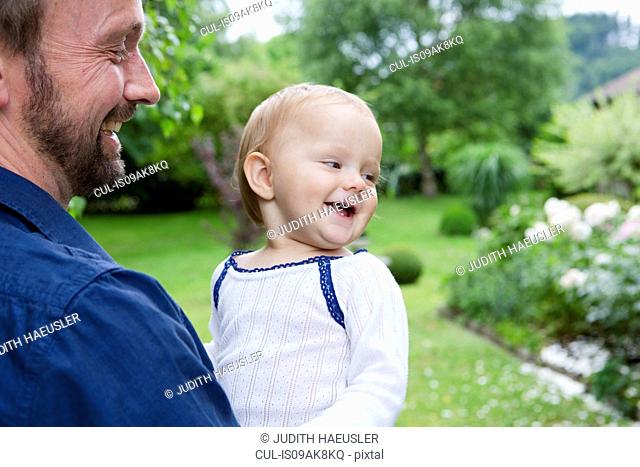 Father carrying baby daughter in garden