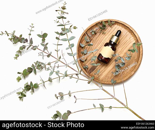 brown glass bottle with a pipette and an empty glued label on a wooden board, next to a branch of eucalyptus