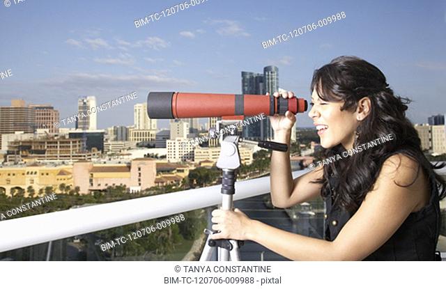 Hispanic woman looking through telescope on balcony