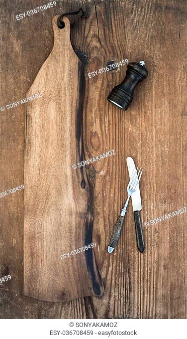 Kitchen-ware set. Old rustic serving board, knive and fork, pepperbox on a old wooden background, top view