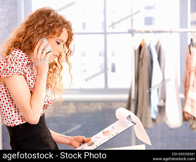 Pretty fashion designer working in office using mobile phone