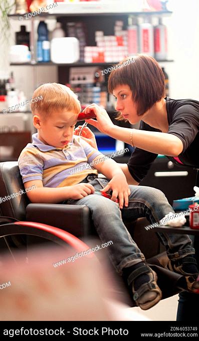 Little boy at the hairdresser sitting staring down at the floor as the stylist carefully trims his hair