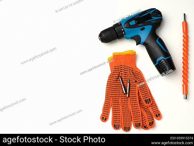 pair of orange textile work gloves and a portable drill on a battery lie on a white table, copy space