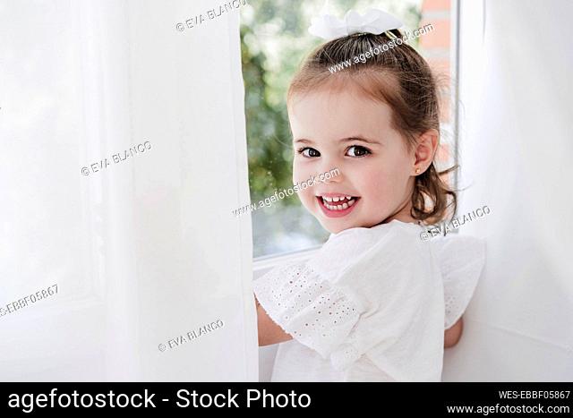 Happy cute girl standing by window at home
