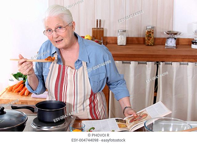 Elderly woman cooking dinner with the help of a recipe