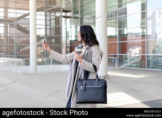 Female entrepreneur taking selfie through mobile phone on footpath