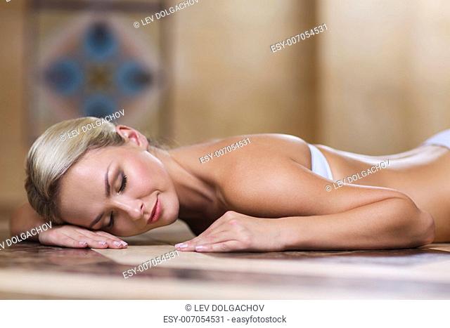 people, beauty, spa, healthy lifestyle and relaxation concept - beautiful young woman lying on hammam table in turkish bath