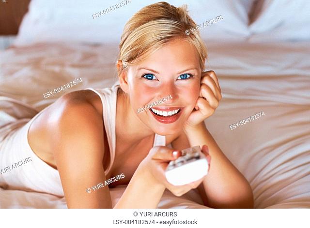 Portrait of beautiful young woman watching television in bed holding a remote control