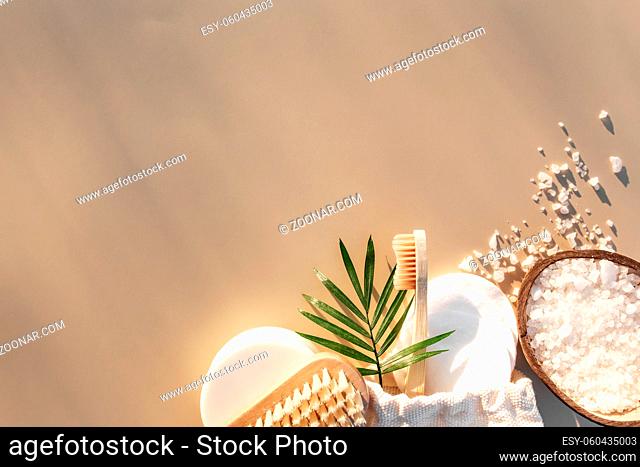 Bath accessories flat lay on beige background with sun shadow effect. Healthcare concept, wooden tooth brush, foot brush, cotton pads, soap