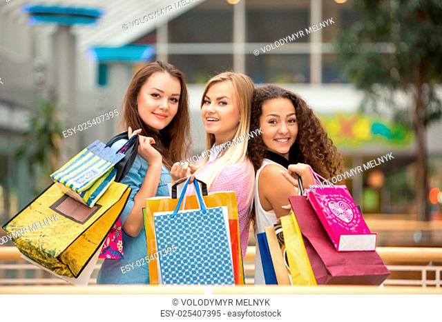 shopping, sale, happy people and tourism concept - three beautiful girls with shopping bags in mall