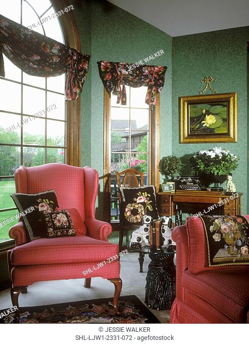 SITTING ROOMS AND AREAS: Victorian sitting area with pink/red wing back chairs and floral pattern pillows and valance. Green textured wallpaper or sponge...