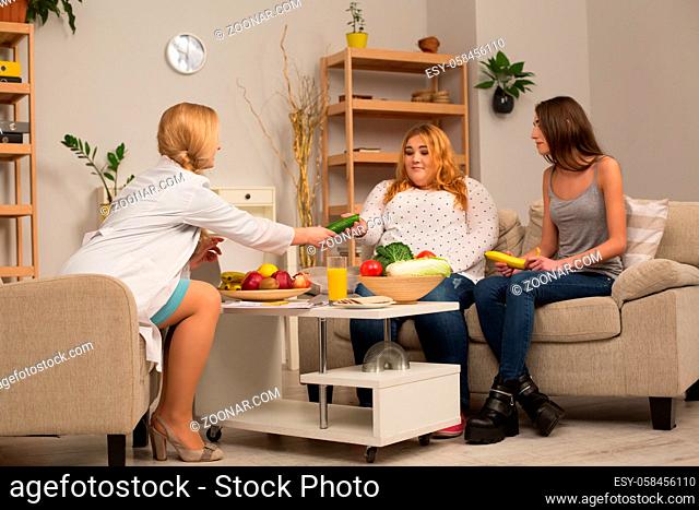 Dietitian consultancy. Doctor giving cucumber to overweight patient