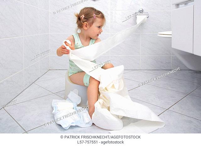 Llittle girl sitting on Potty in bathroom, unrolling toilette paper while doing potty training, playing and fooling around