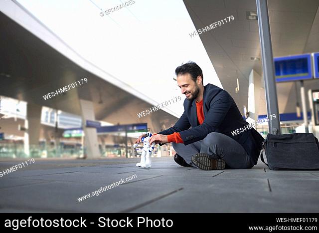 Smiling entrepreneur looking at robot while sitting on railroad platform