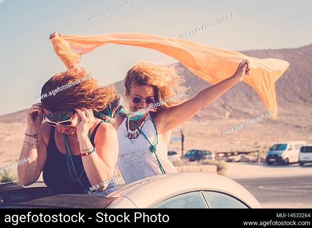 Couple of adult women friends have fun together standing outside the roof of their convertible car. Concept of happy lifestyle and travel tourism holiday summer...