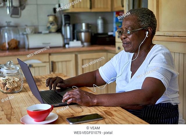 Senior woman sitting at kitchen table using laptop