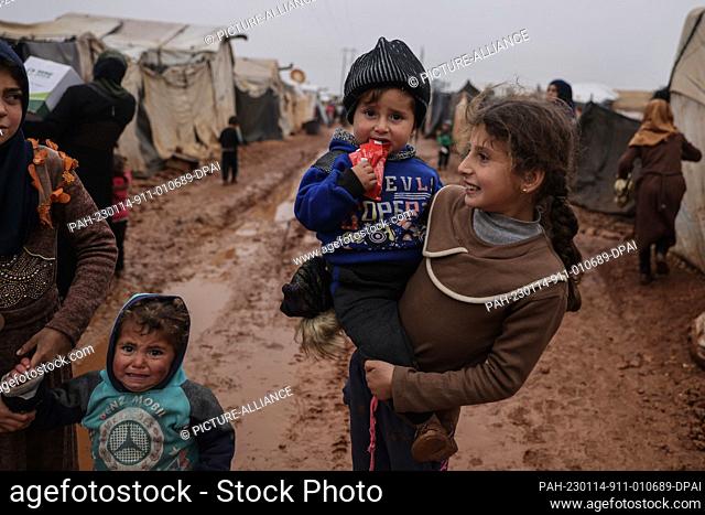 14 January 2023, Syria, Idlib: Syrian children stand to receive aid in a camp for the displaced during the rains. Harsh winter weather with heavy rainfall and...