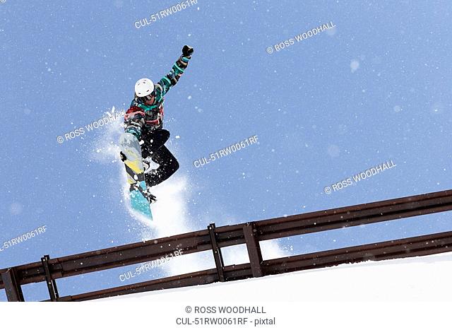 Snowboarder jumping over metal railing
