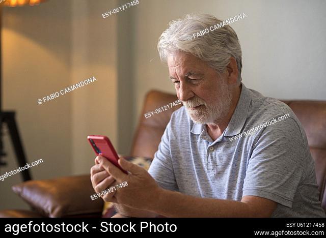 Mature handsome man text and write message on the smartphone - elderly people use cellular to chat sit down on the sofa at home - one retired people indoor...