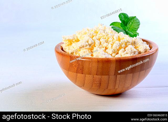 Organic cottage cheese is served in a wooden bowl with a sprig of fresh mint. Concept of healthy eating. Copy space