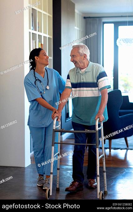 Biracial female physiotherapist talking and assisting caucasian senior man in walking with walker