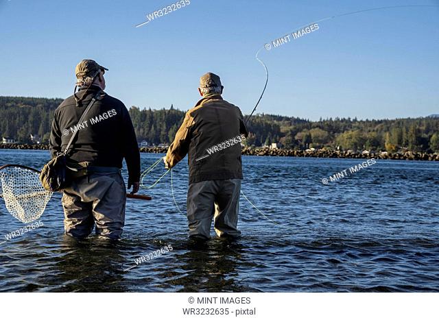 A guide advises his client while fly fishing in salt water for searun coastal cutthroat trout and salmon in northwest Washington State, USA