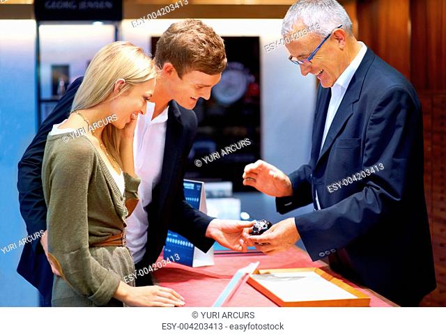 Mature jeweller showing a designer wristwatch to a happy young couple
