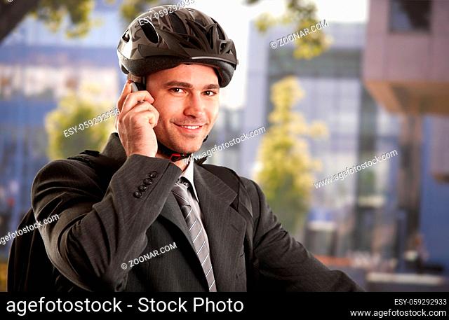 Portrait of young businessman wearing bike helmet, talking on mobile phone, outdoors