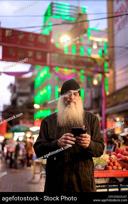 Portrait of mature handsome bearded tourist man exploring Chinatown in Bangkok city at night