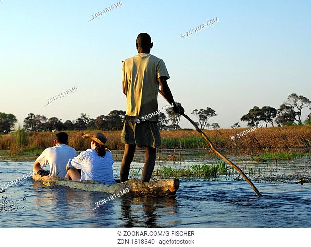 Kahnfahrer mit Touristen im traditionellen Mokoro Einbaum auf Exkursion im Okavango Delta, Botswana / Poler with tourists in a traditional mokoro logboat on...