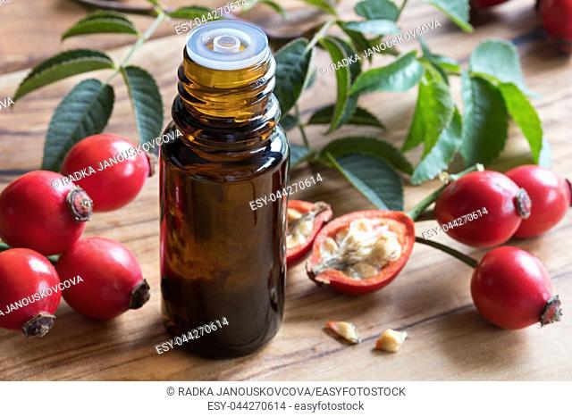 A bottle of rosehip seed oil on a wooden table, with fresh rosehips in the background