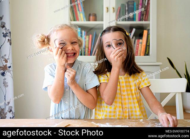 Girls looking through heart shaped cookie cutter at home