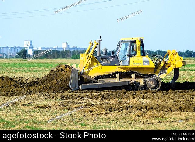 Russia, Temryuk - 15 July 2015: The yellow tractor with attached grederom makes ground leveling. Work on the drainage system in the field